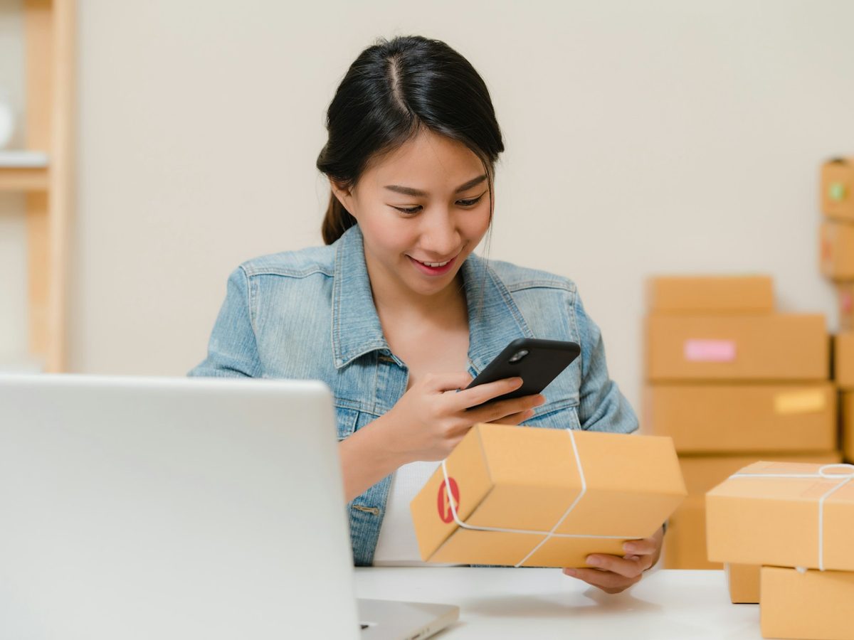 Dueña de un negocio revisa un aviso en el celular mientras prepara un envío